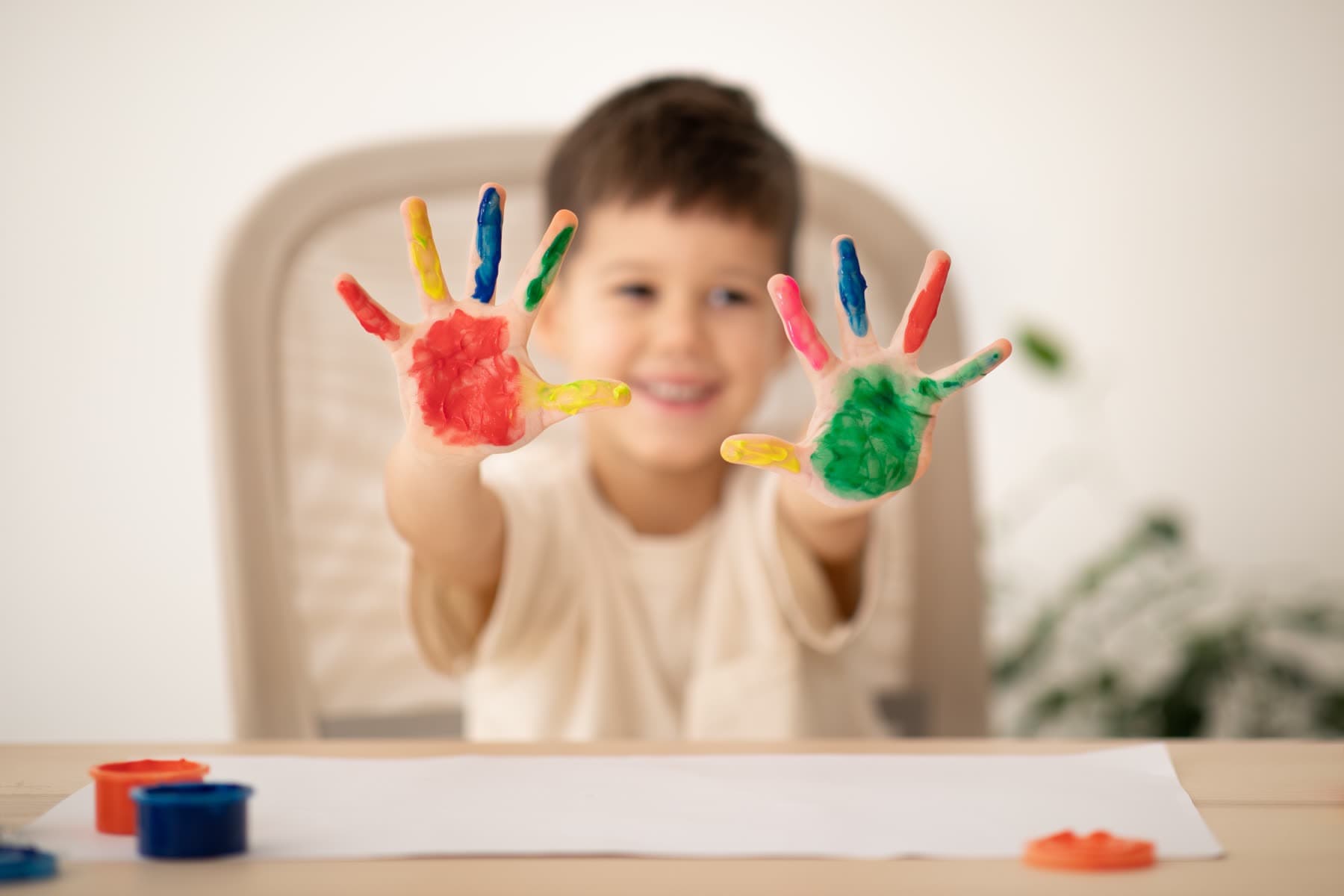 Un niño muestra las palmas de las manos pintadas de rojo, verde y azul después de una clase de pintura.